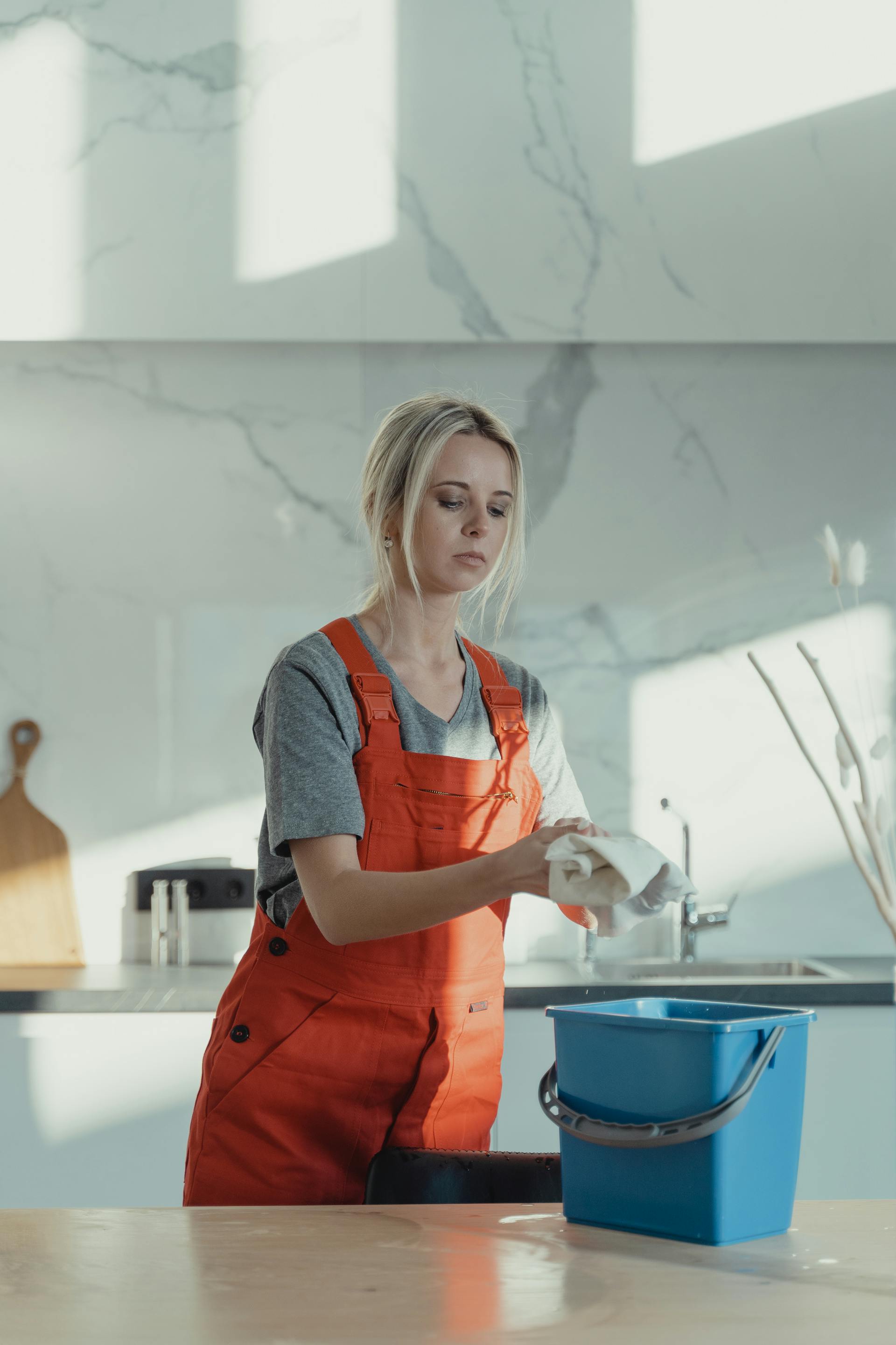 Clean Tech in an orange work apron wiping down a kitchen counter, cleaning bucket at the ready
