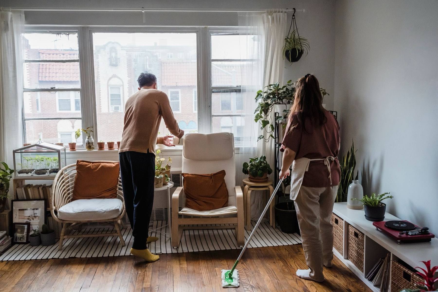 Two people cleaning a bright family living room with hardwood floors